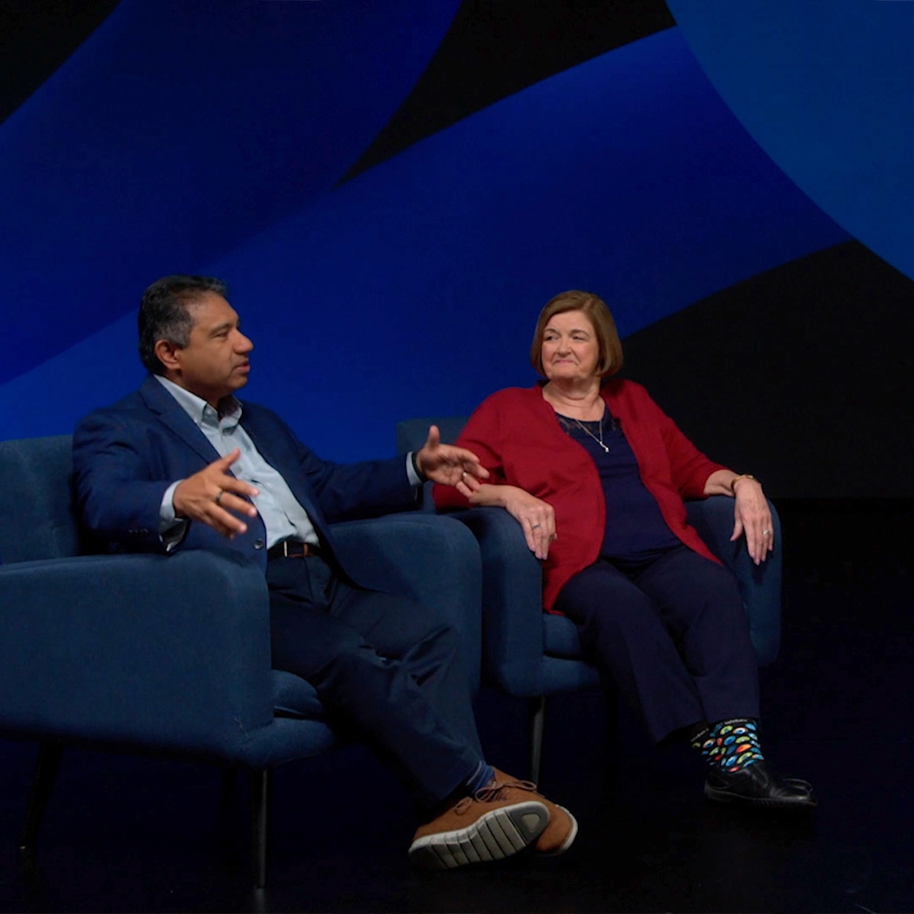 Two speakers chat onstage during their WebexOne 2022 talk, sitting in blue armchairs.