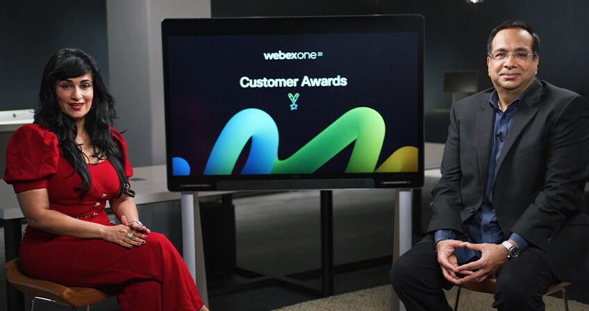 Cisco's Aruna Ravichandran and Gaurav Verma sit on either size of a screen that says WebexOne 22 customer awards.