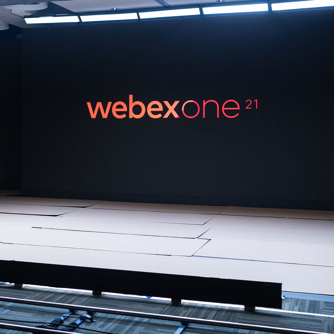 A large stage with a black backdrop that has the words WebexOne 21 displayed on it in orange and red font